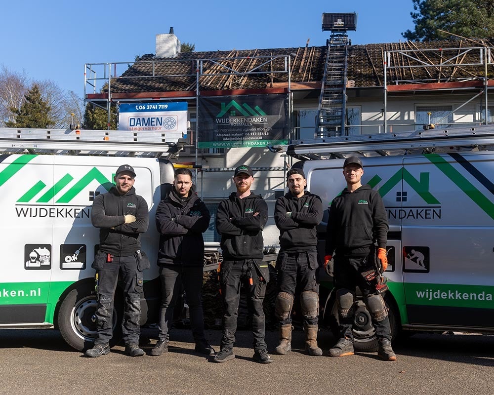 Team van Wijdekkendaken poseert voor twee bedrijfsbussen bij een woning waar een dakrenovatie bezig is.