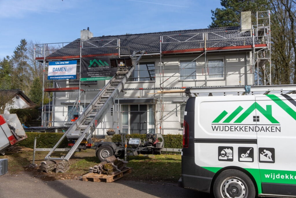 De bedrijfsbus van Wijdekkendaken staat geparkeerd voor een woning met steigers en een daklift tijdens een dakrenovatieproject.
