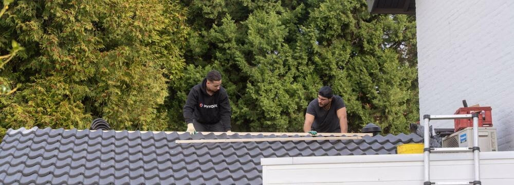 Twee dakdekkers werken aan een antraciet pannendak