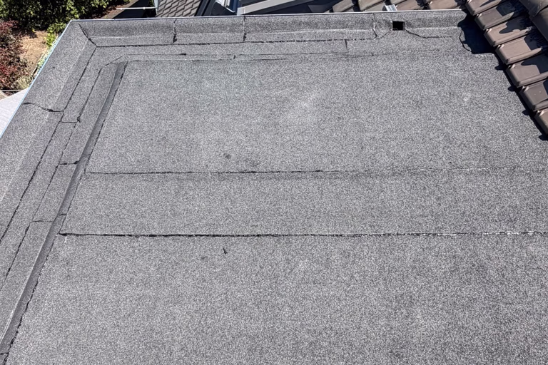 Afgewerkt bitumen plat dak naast een dakraam